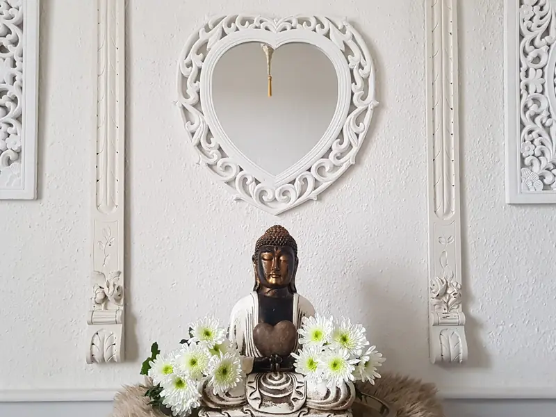 Buddha-Figur mit weissen Blumen vor einer weissen Wand