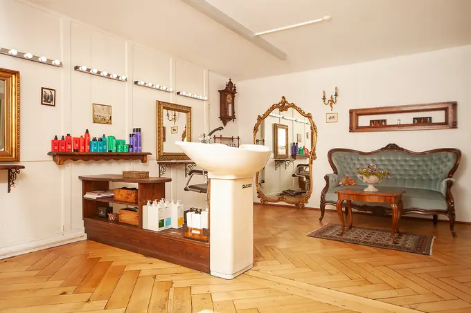 Der Salon: Waschbecken, goldene Spiegel und ein grünes Sofa auf Parkett